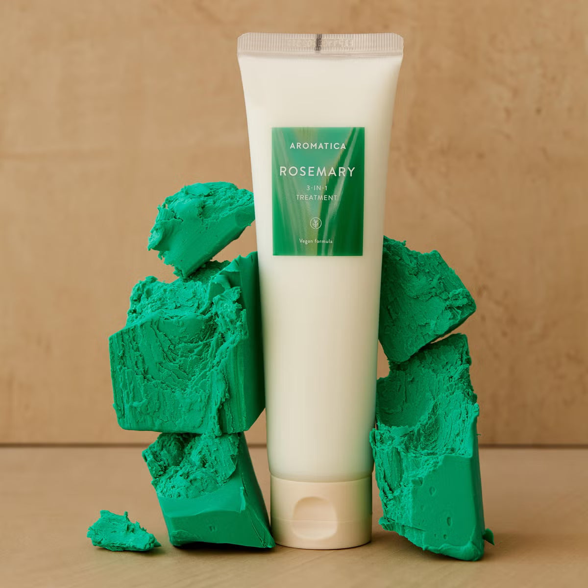 Tube of Aromatica Rosemary treatment surrounded by green textured blocks on a beige background