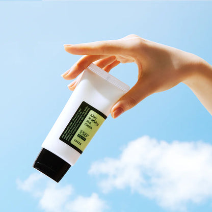 Hand holding COSRX Aloe Soothing Sun Cream SPF50+ PA+++ against blue sky showing lightweight Korean sunscreen for daily sun care
