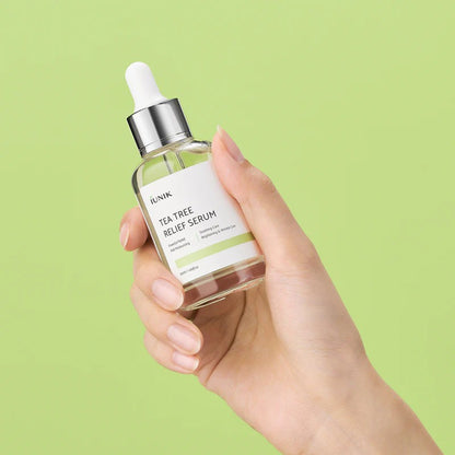 Hand holding the iUNIK Tea Tree Relief Serum bottle against a green background