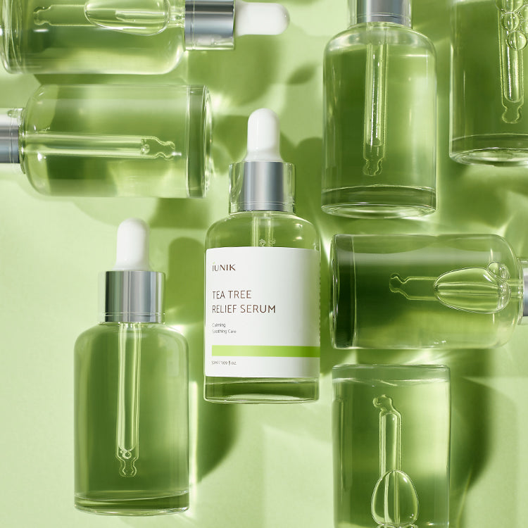 Several iUNIK Tea Tree Relief Serum bottles grouped together on a green background