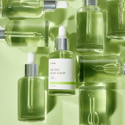 Several iUNIK Tea Tree Relief Serum bottles grouped together on a green background
