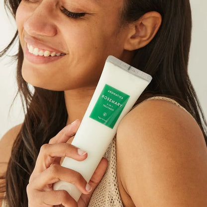 Woman holding a tube of Aromatica Rosemary hair treatment